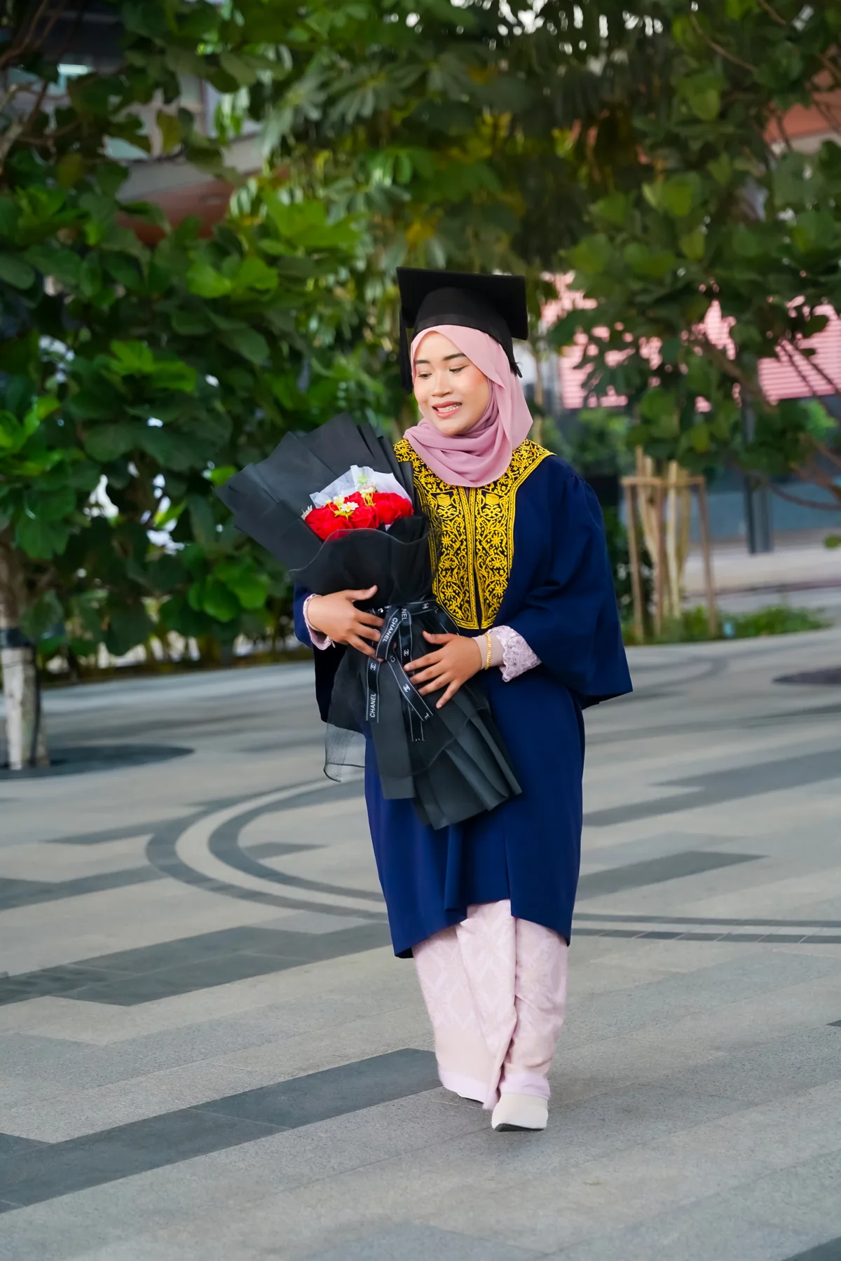 Graduan berjubah biru memegang sejambak bunga di luar