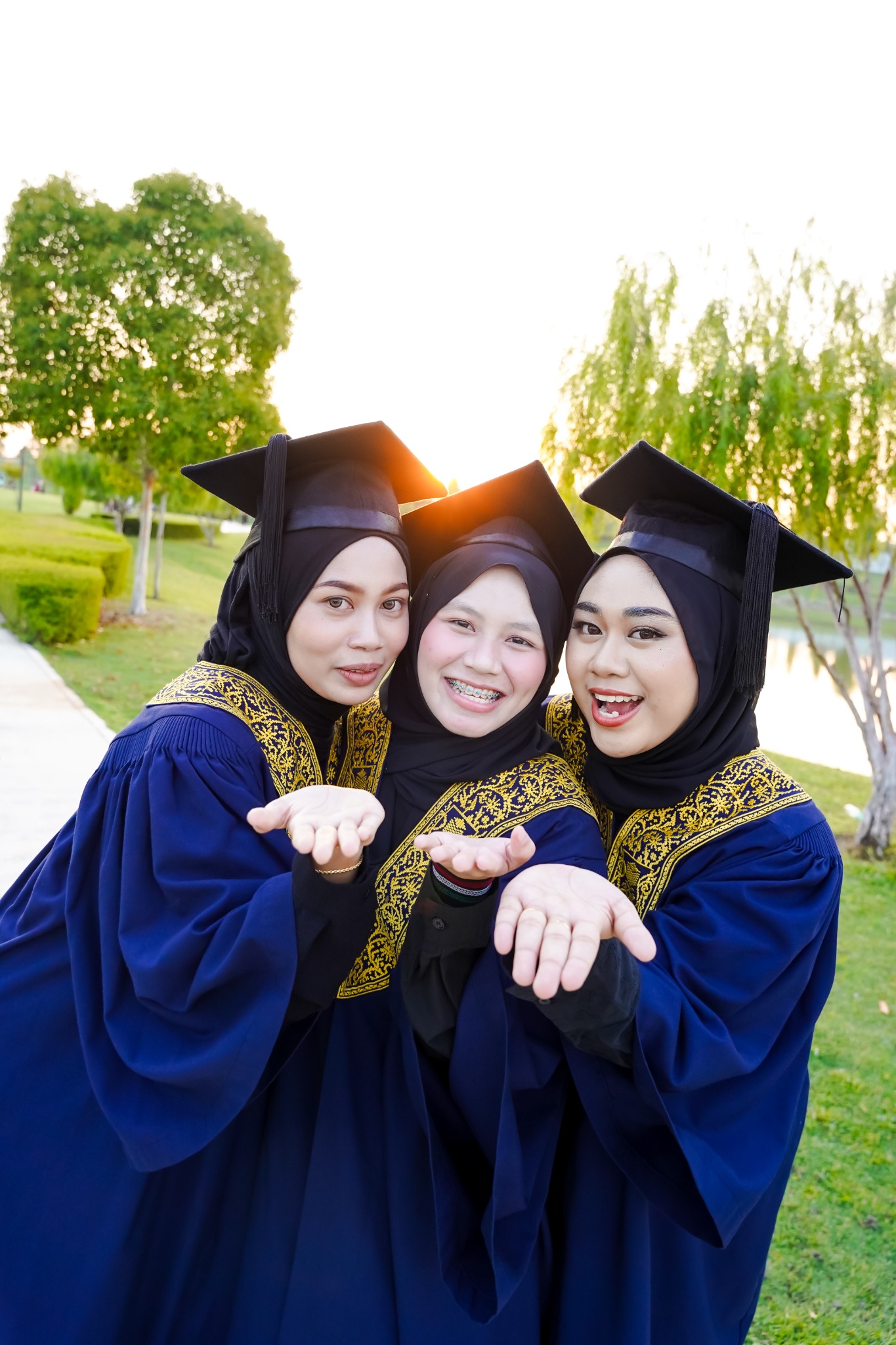 Tiga rakan berjubah biru tersenyum rapat bersama dalam sesi Pre Convo.