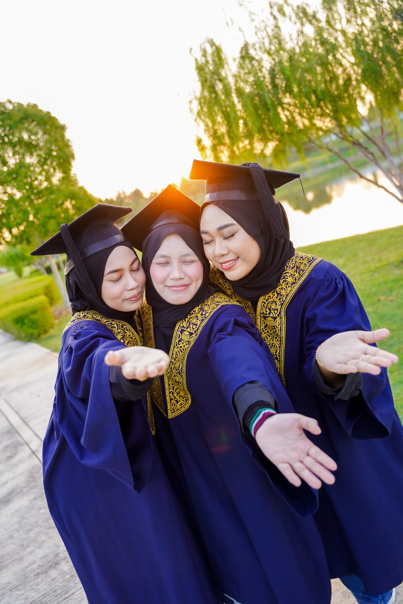 Tiga rakan berjubah biru bergambar rapat dalam cahaya petang semasa sesi Pre Convo.