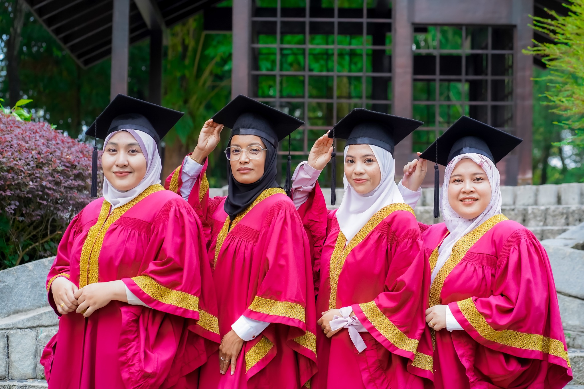 Empat rakan berjubah merah jambu bergambar bersama dengan topi konvokesyen.
