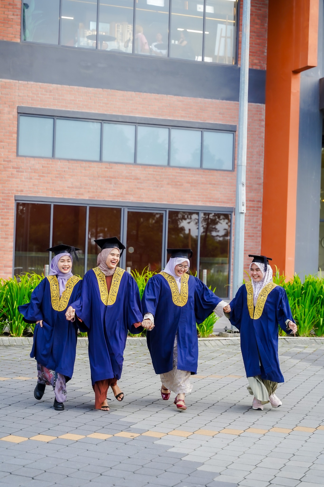 Empat rakan berjalan sambil berpegangan tangan dan ketawa dalam sesi Pre Convo.